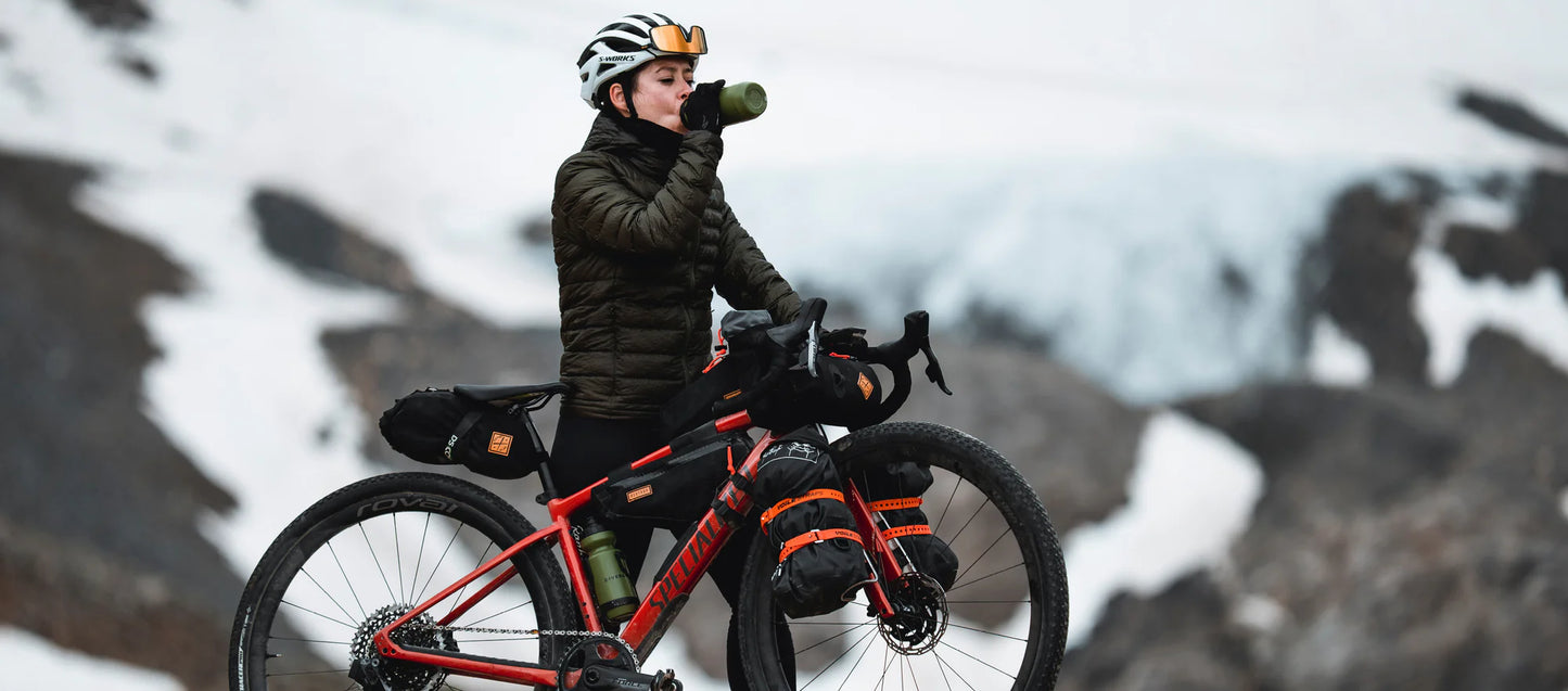 Een fietser met een volledig bepakte gravelbike inclusief Restrap tassen neemt een pauze in een ruig, bergachtig landschap.
