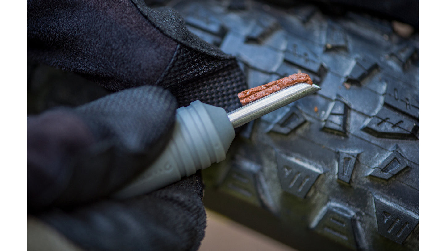 Close-up van een hand met handschoen die een tubeless reparatieplug in de Blackburn Plugger tool steekt.