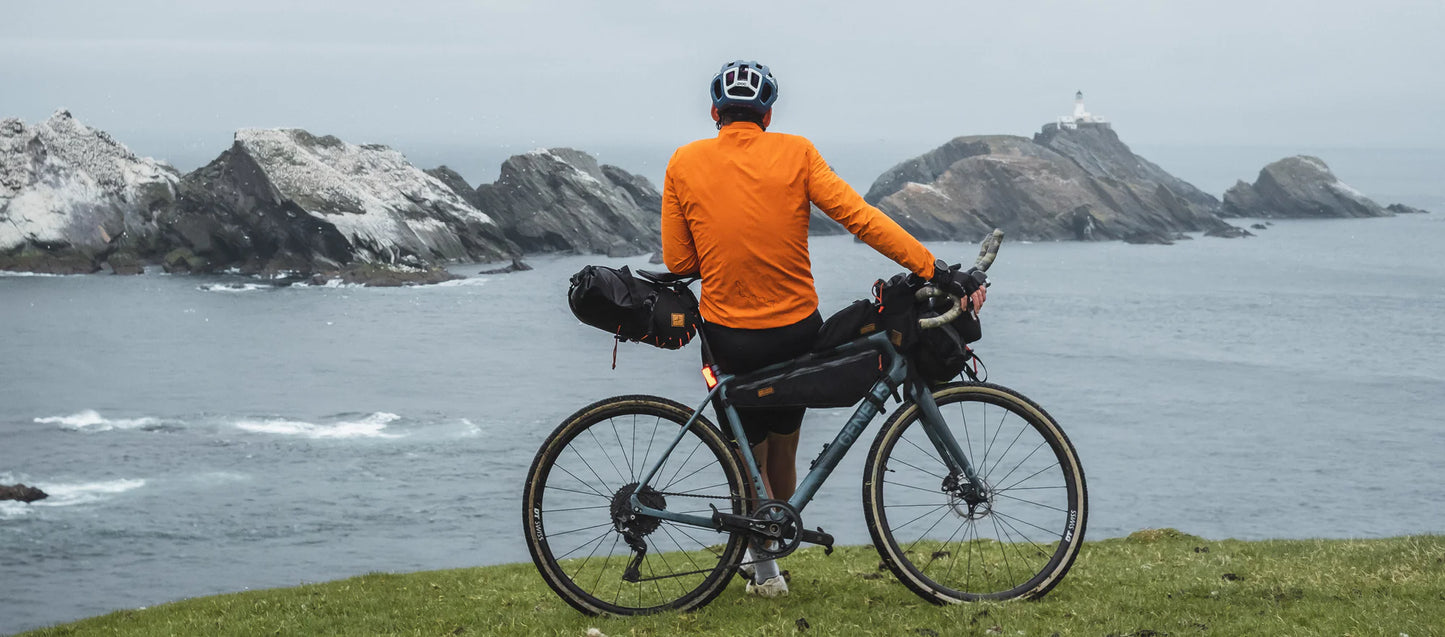 Fietser met een volgeladen bikepacking-fiets, inclusief de Restrap Frame Bag Large, kijkt uit over de zee.