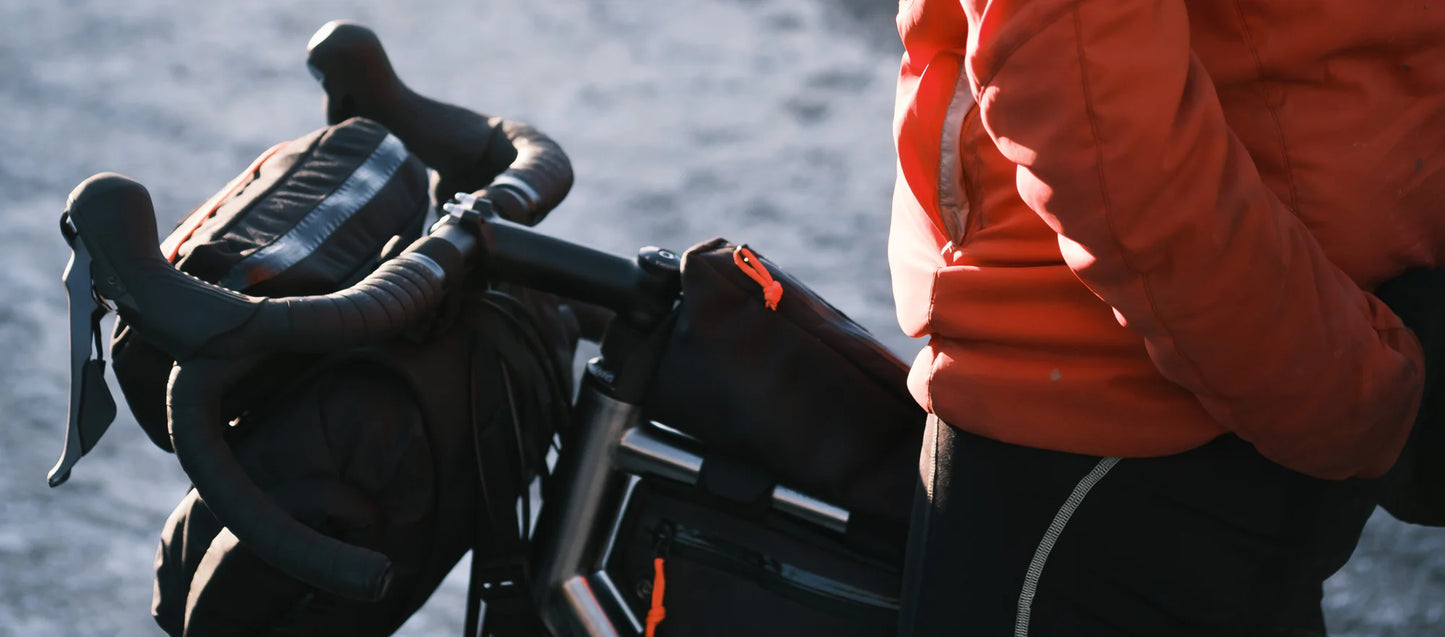Lifestyle-foto van een fietser met een oranje jas naast een fiets met de Restrap Top Tube Bag.